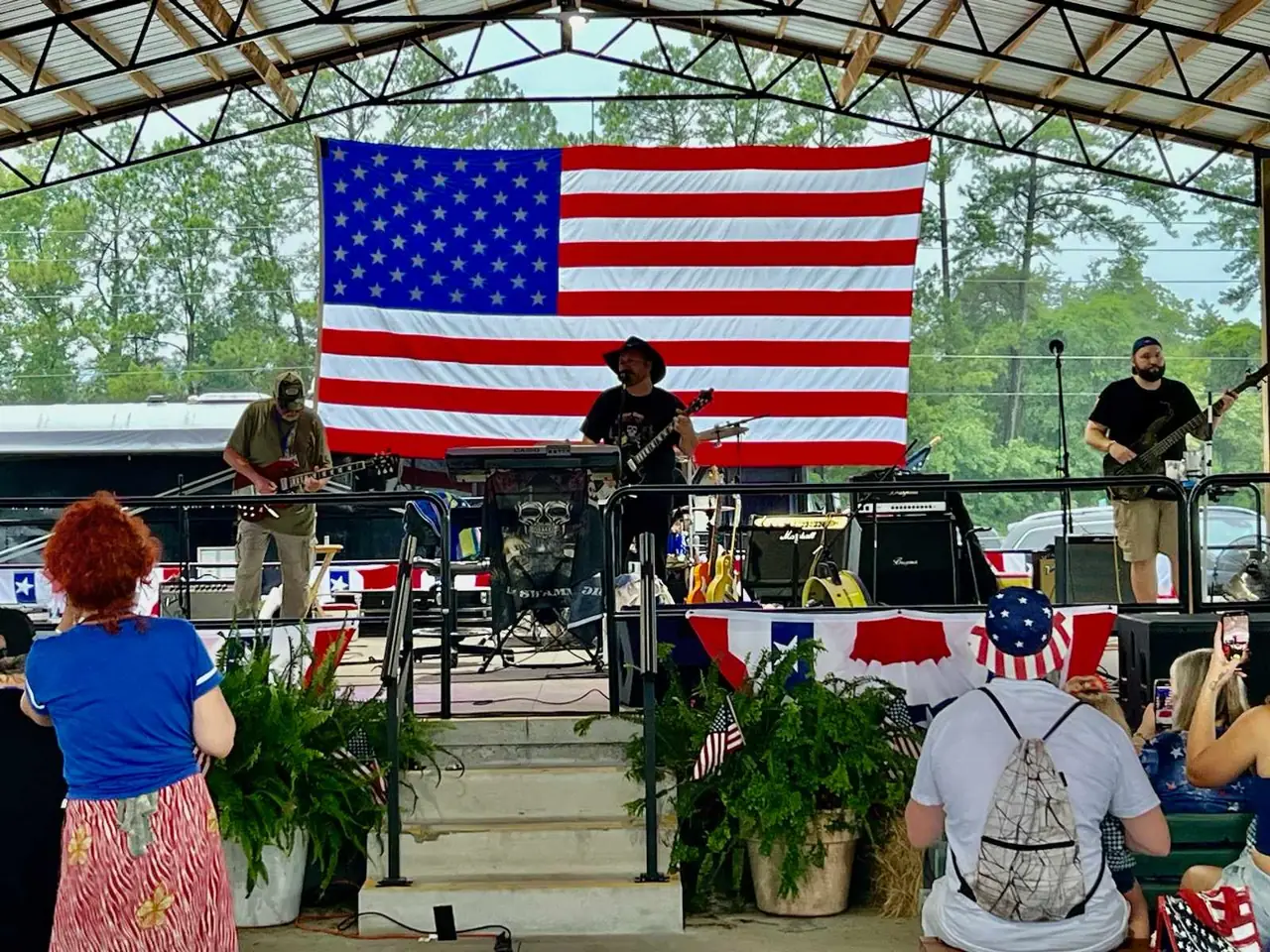 Band performing on an outdoor festival stage beneath a large American flag