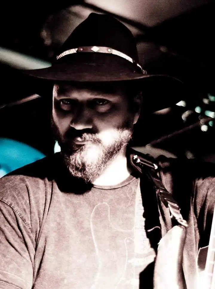 Black-and-white portrait of a man in a hat holding a guitar
